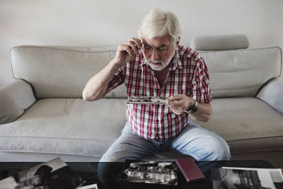 Senior man looking at vintage photographs while sitting on sofa at home