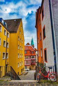 Narrow footpath amidst houses against cloudy sky