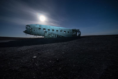 Abandoned airplane at beach against sky during night
