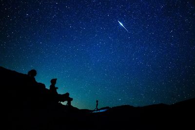 Silhouette people on mountain against stars in sky