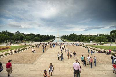 Group of people walking on road against cloudy sky