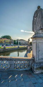 Statue by river against buildings in city against sky