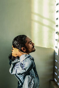 Side view of young woman looking away against wall