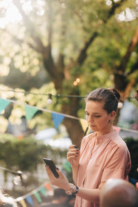 Young woman talking through earphones while standing in balcony during party