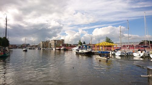 Boats moored at harbor against sky in city