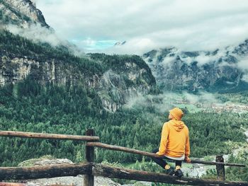 Rear view of man sitting on fence against mountain