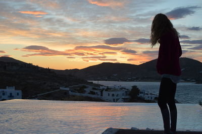 Rear view of woman standing by sea against sky during sunset