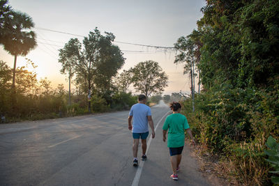 Rear view of people walking on road against trees