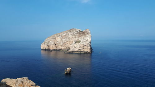 Rock formation in sea against blue sky