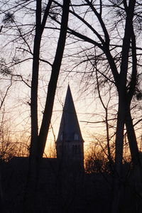 Bare trees against sky at sunset