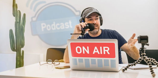 Radio host in headphones recording podcast in studio man streaming audio using microphone and laptop