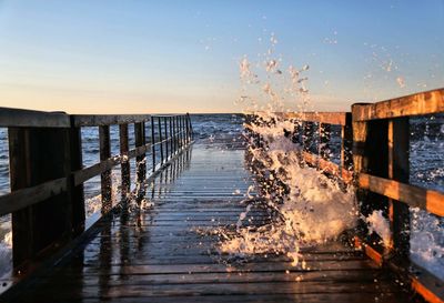 Wooden pier over sea against clear sky during sunset