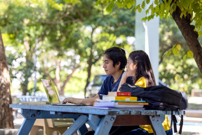 Couple of students sitting and using laptop in outdoor university doing some online research