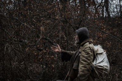 Side view of man gesturing while standing against trees in forest