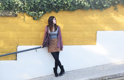 Full length of young woman looking up while standing against wall