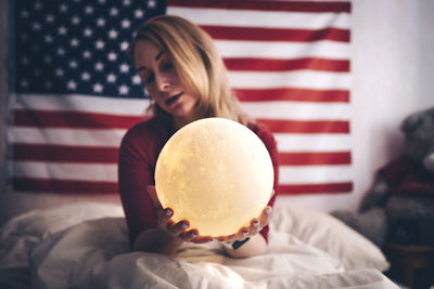 Woman holding illuminated globe while sitting on bed at home