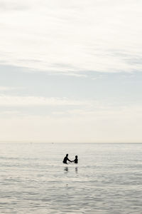 Silhouette people in sea against sky