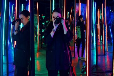 Woman photographing through camera reflecting in illuminated mirrors during event