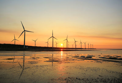 Wind turbines on land against sky during sunset