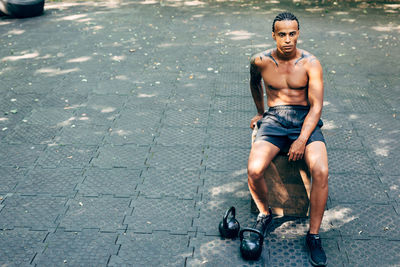 Full length of shirtless young man sitting in city