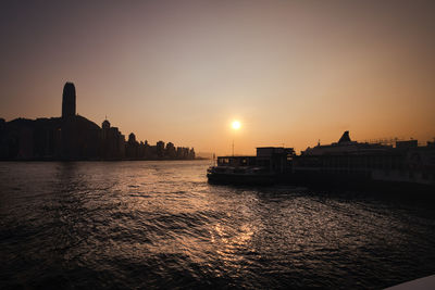 Silhouette of buildings by river during sunset