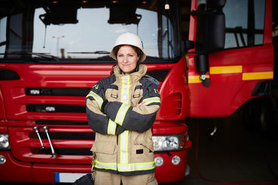 Portrait of confident female firefighter standing with arms crossed against fire engine at fire station