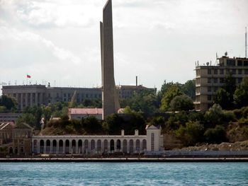 Buildings at waterfront against cloudy sky