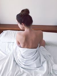 Rear view of naked woman sitting on bed at home