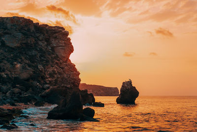 Rock formation in sea against sky during sunset