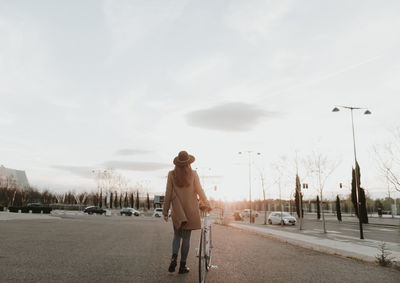 Young hipster woman going with a bicycle during sunset