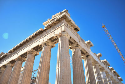 Low angle view of historical building with columns against blue sky with crane in the background.