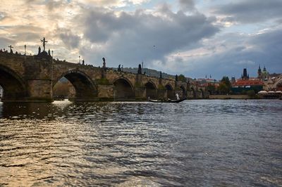 Arch bridge over river by buildings against sky