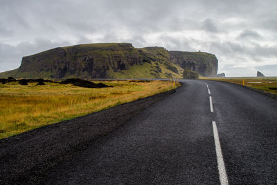 Road by grassy field against cloudy sky 