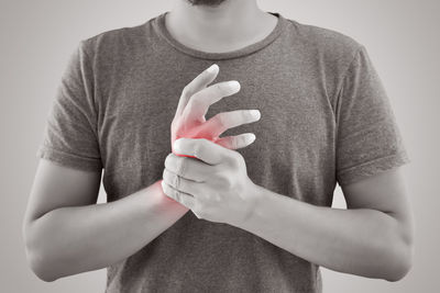 Midsection of man with wrist pain standing against gray background