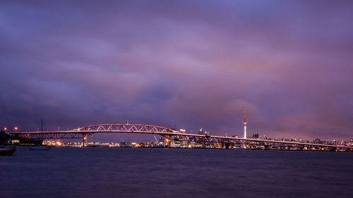 Illuminated bridge over river against cloudy sky