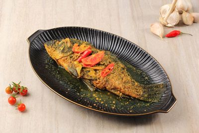 Ikan pesmol or pesmol fish with yellow curry, close up on wooden table with copy space for text