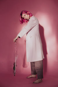 Portrait of young woman holding plastic purse while standing over colored background