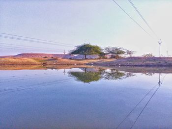 Reflection of trees on electricity pylon against sky