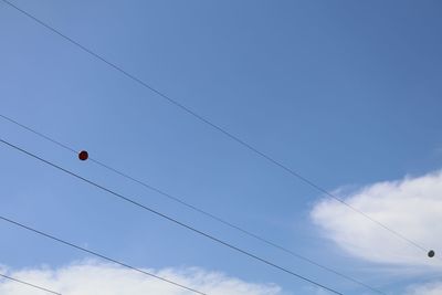 Power cables against cloudy sky