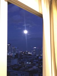 Illuminated buildings in city against sky seen through window