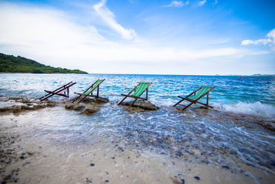 Abandoned deck chairs at beach against sky