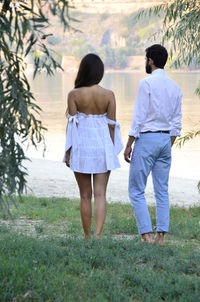 Rear view of couple standing on grassy field against lake