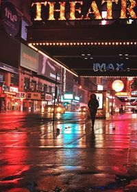 Man walking on illuminated city street during rainy season