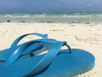 Close-up of shoes on beach against blue sky