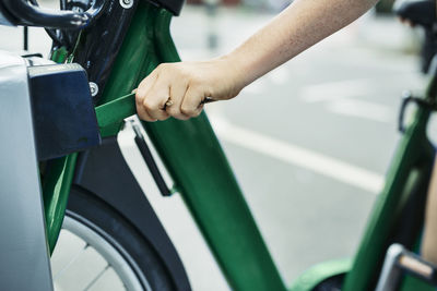 Cropped image of woman unlocking bicycle from rack at street