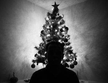 Rear view of silhouette man against illuminated christmas tree