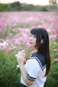 Side view of young woman standing amidst flowering plants