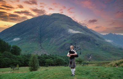 Full length of bagpiper standing on field against mountain