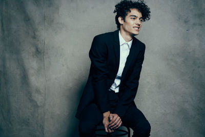 Young man looking away while sitting against wall