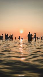 Silhouette people standing in sea against clear sky during sunset